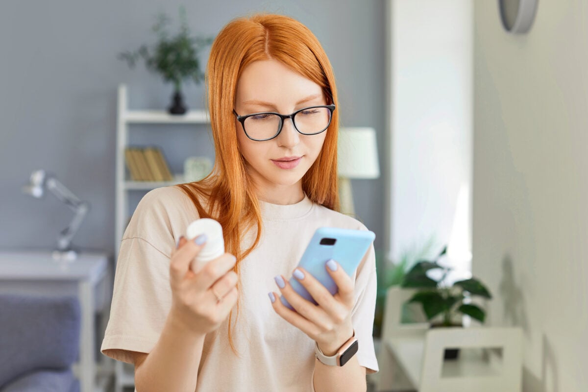 Focused woman holds a bottle of pills and searches for information about medication online using phone. Healthcare research and the use of the internet to find important medical information.