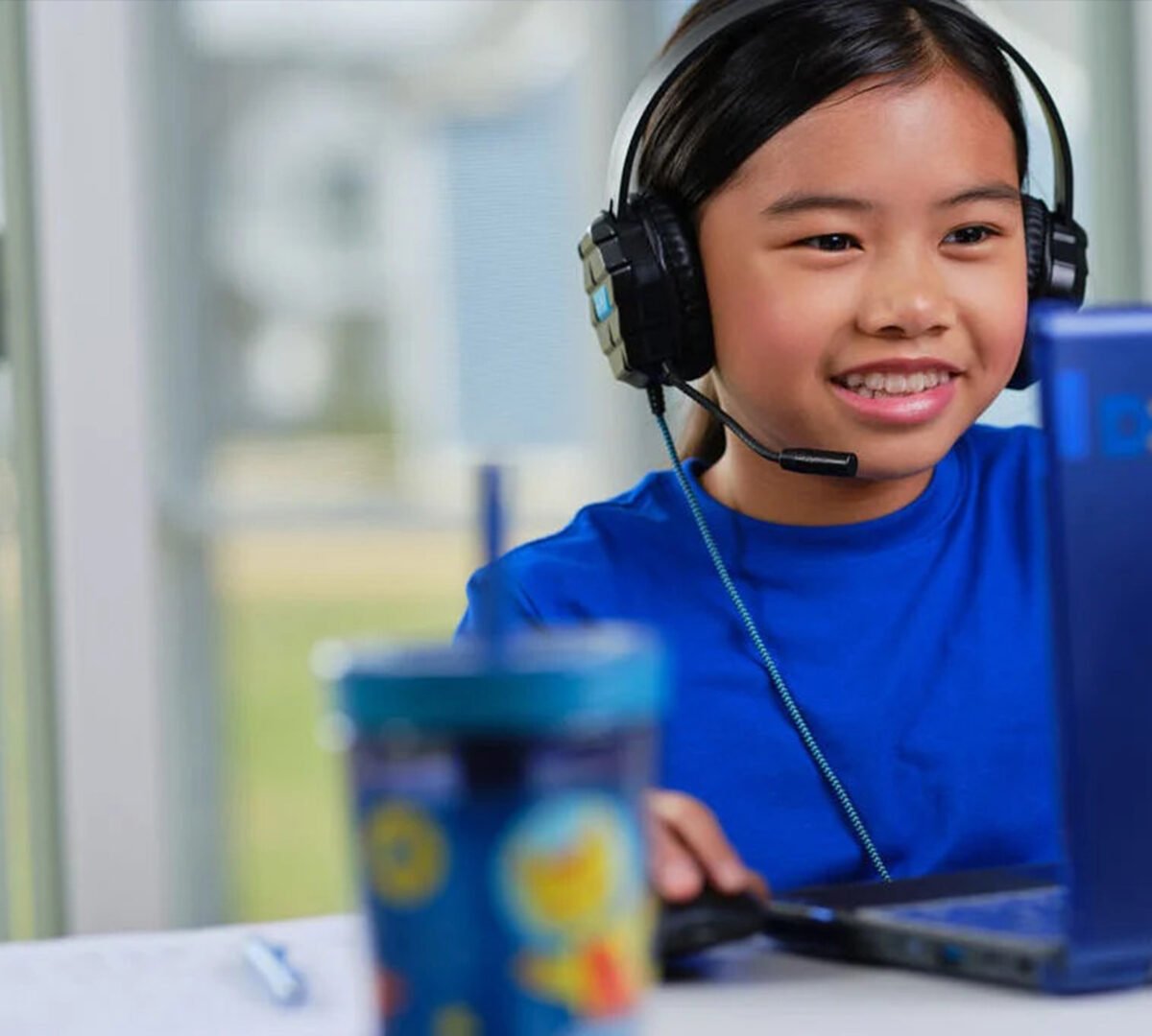 Young girl at a laptop at her desk with headphones on.