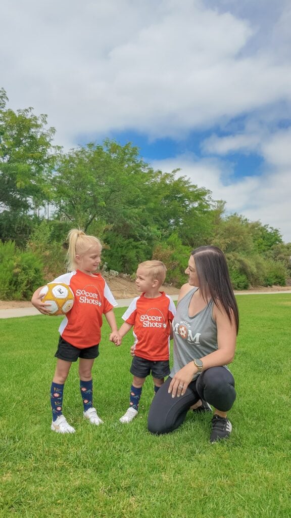 two children playing soccer with mother