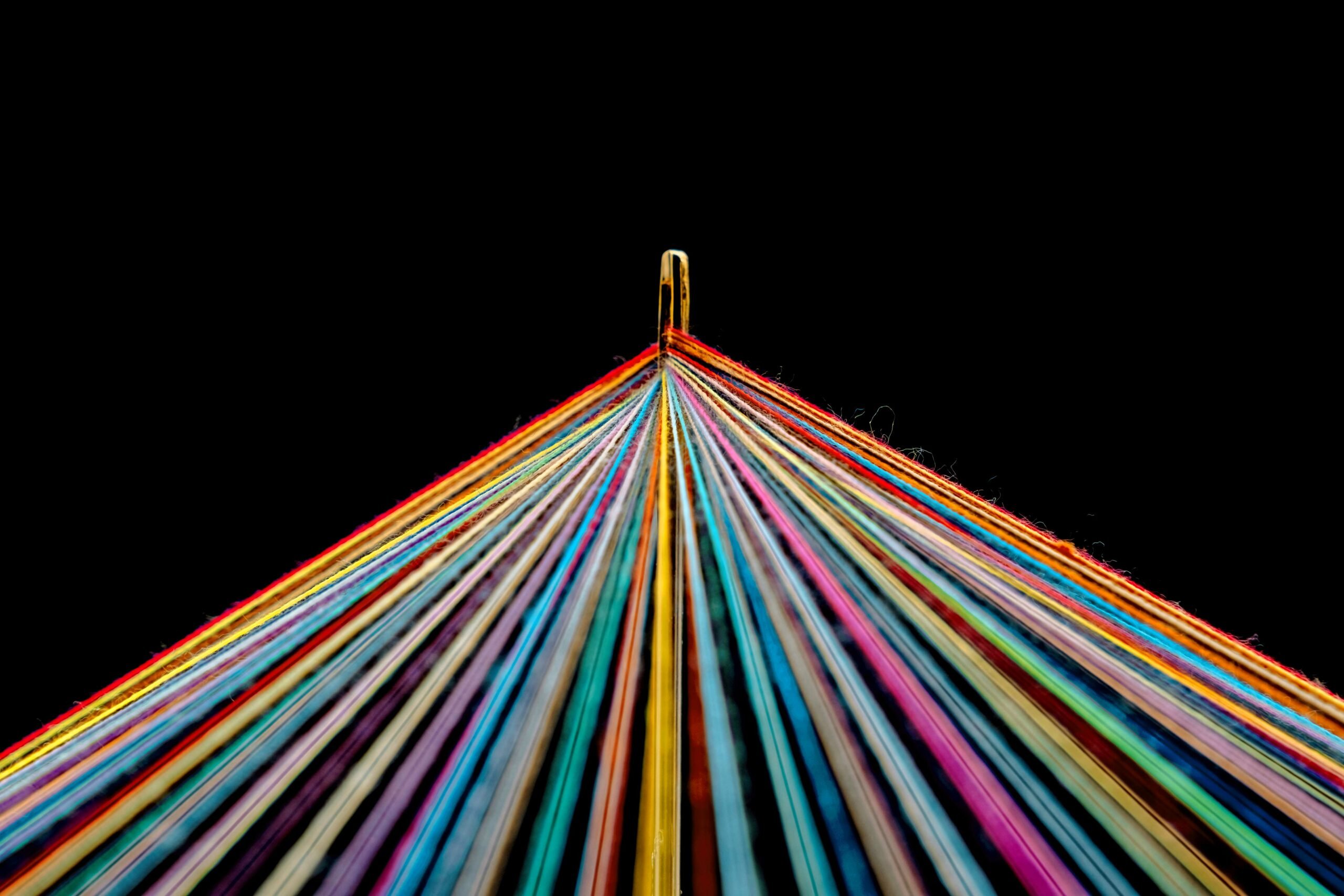 Rainbow Colored Threads Through Needle Eyelet on black background
