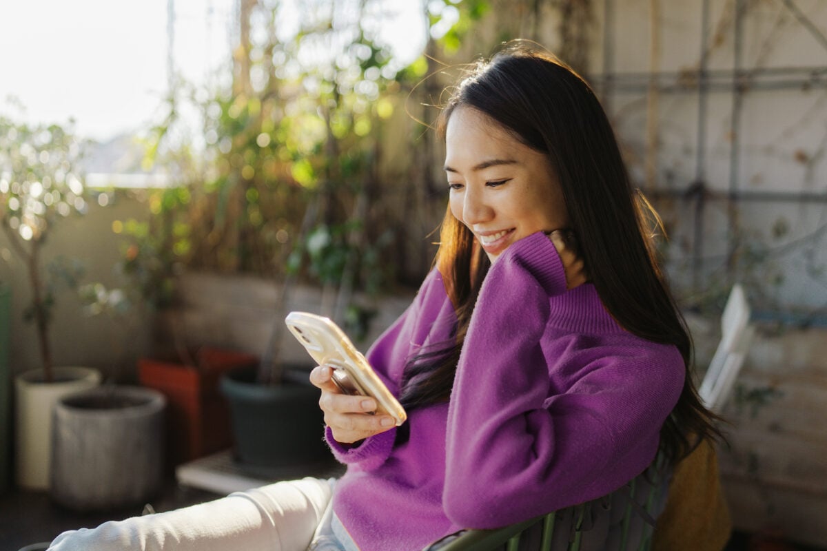 Photo of a young Japanese woman, checking up her social media accounts and reading news online while resting on the balcony of her apartment