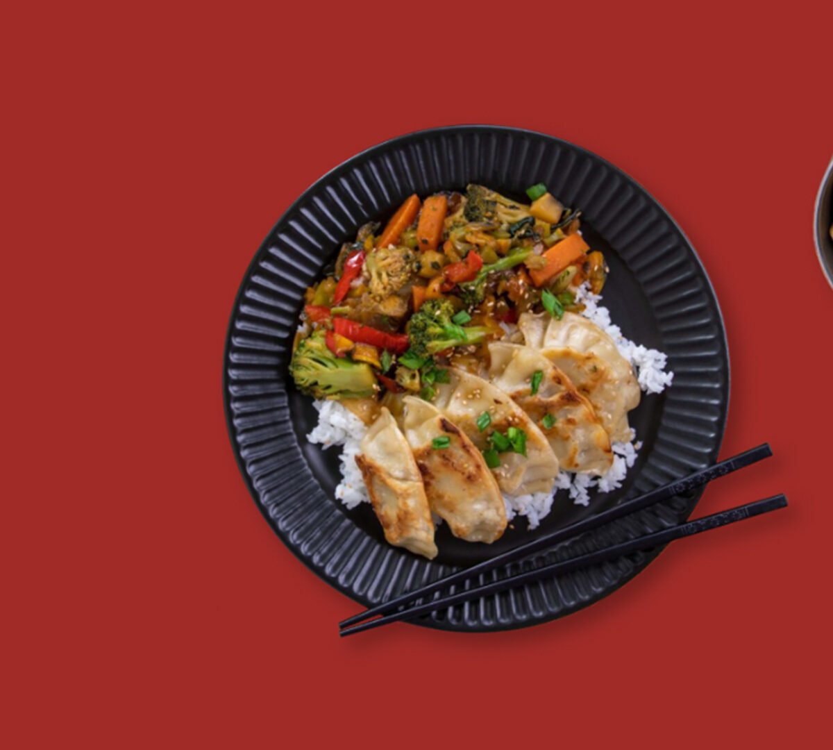 A plate of glorious food on a red background with chopsticks.